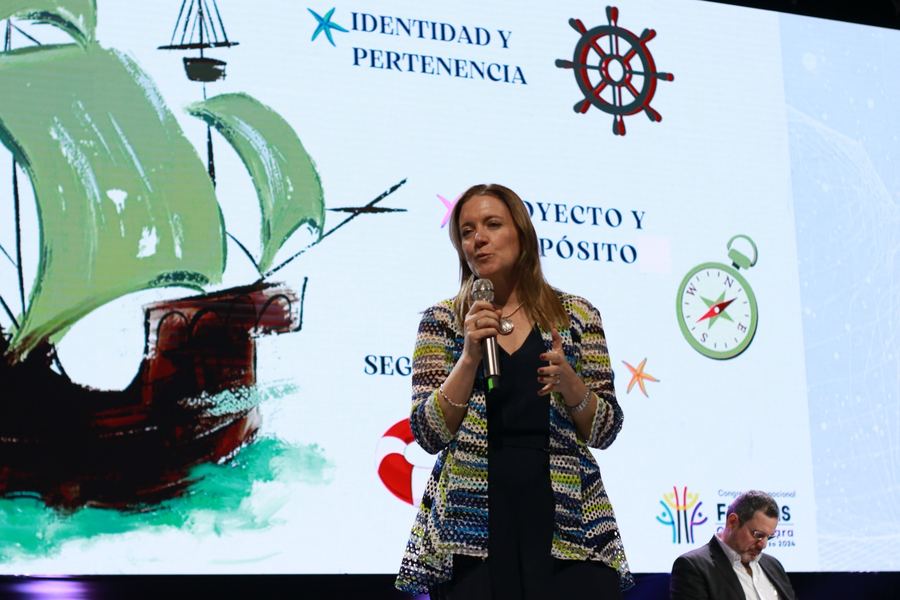 Dany Teruggi habla con micrófono en el escenario del Congreso Internacional de las Familias, frente a una pantalla con un barco y las palabras identidad, pertenencia y proyecto.