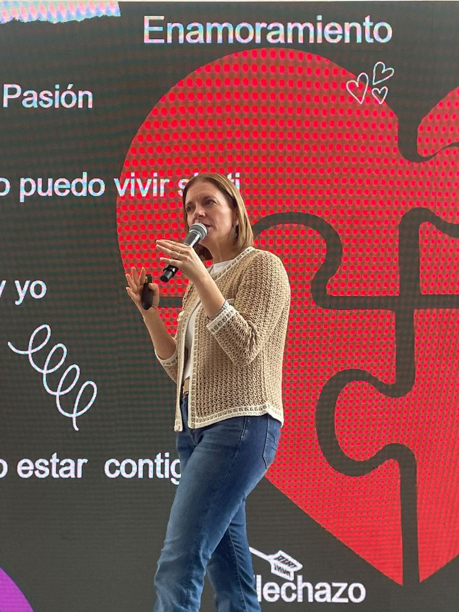 Dany habla con micrófono frente a una pantalla roja con la palabra «Enamoramiento».