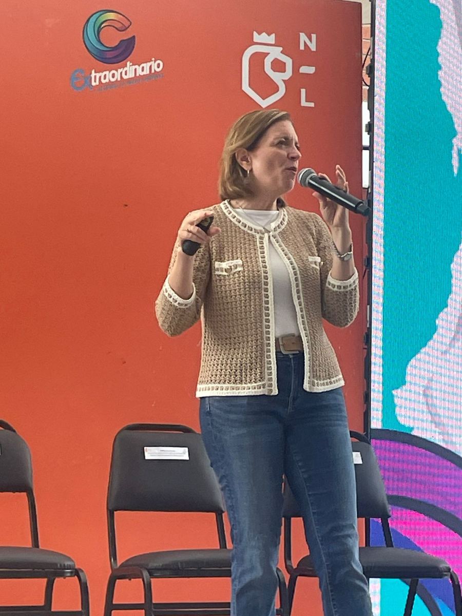 Dany, de pie en un escenario naranja, habla con micrófono a un auditorio.